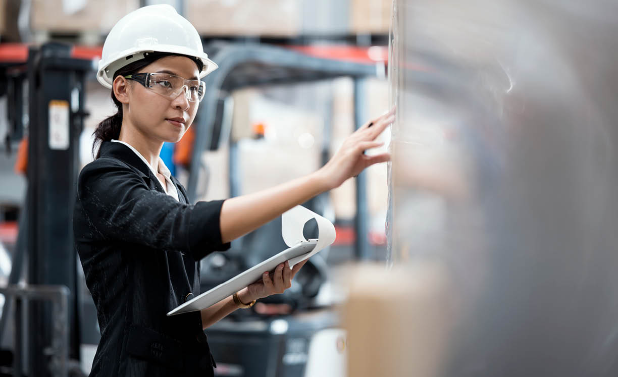 A young female in a polo shirt uniform checking the product in a shelf rack. Asian staff taking inventory in a distribution warehouse. Warehouse and Supply Chain Management Solution.