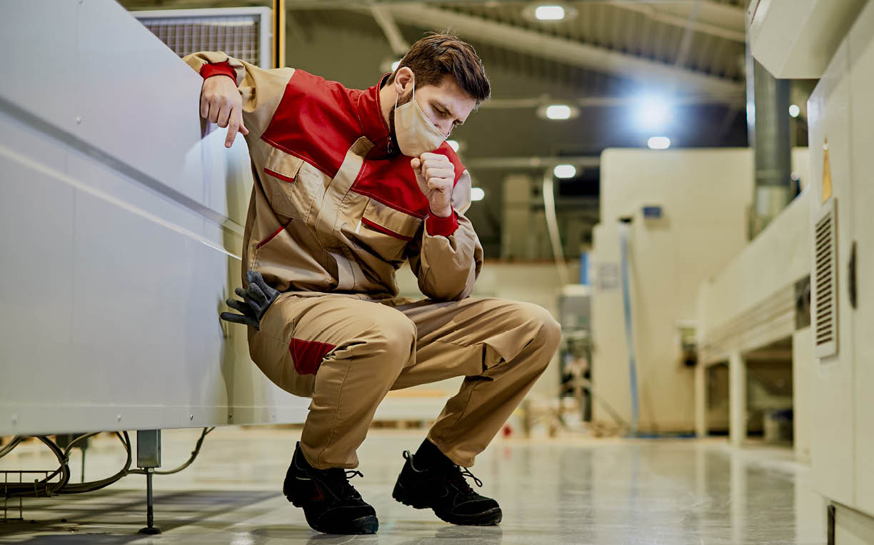 Factory worker with face mask feeling ill and coughing while working at production facility.