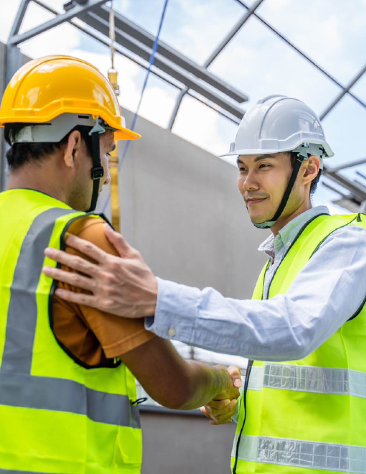Asian structure engineer and worker making handshake on building working site. All people wearing safety hardhat during walking in construction workplace. Business deal, merger and acquisition concept